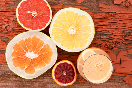 Glass of freshly liquidised grapefruit juice with halved fresh grapefruit, pomelo and ruby grapefruit on a grungy wooden background with red peeling paint and copyspace, overhead viewの写真素材