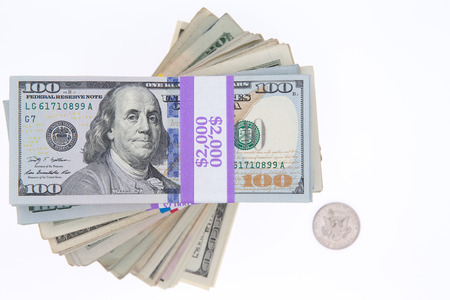 Stacked bundles of American 100 dollar bills in bank wrapping forming a spiral viewed from above isolated on white with a single dollar coin alongside and copyspaceの写真素材