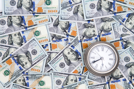 Conceptual financial background of American 100 dollar bills with Benjamin Franklinf facing upwards and a vintage watch depicting timeの写真素材