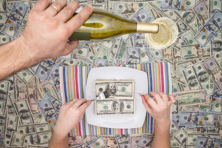 Man eating dollar bills as a servant pours champagne from a bottle overhead on a background of money in a conceptual image of wealth and extravaganceの写真素材