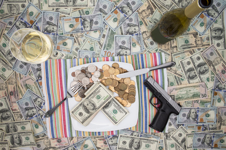 Overhead view of a place setting with a plate of money, a handgun and champagne on 100 dollar bills depicting wealth through crime and racketeering or celebrating a win and keeping it secureの写真素材