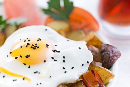 Nutritious fried egg served sunny side up with healthy fresh vegetables including diced potatoes and mushrooms with tomato garnished with fresh parsleyの写真素材