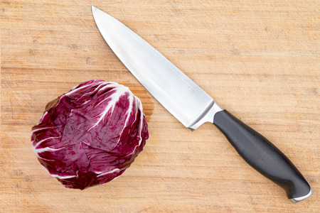 Overhead view of a single cleaned whole raw red radicchio displayed with a kitchen knife on an old bamboo cutting board with copyspace during preparation in the kitchenの写真素材