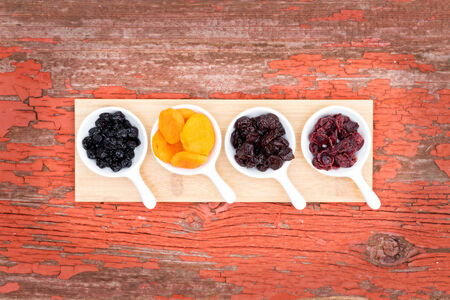 Overhead view of a display on rustic grunge wood of assorted dried berries and fruit in ceramic ramekins with golden apricots, cherries, blueberries and cranberries for a healthy snack or appetizerの写真素材