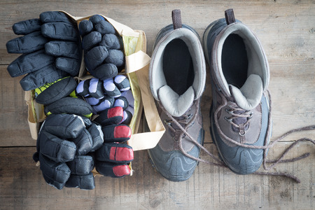 Snow boots with the laces lying free and a bag of winter gloves and mittens standing ready side by side on the floor of a rustic cabin, overhead viewの写真素材