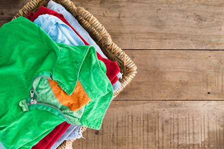 Clean washed unironed summer clothes with a fresh fragrance stacked in a wicker laundry basket with a bright green shirt on top, overhead view on rustic wooden boards with copyspace to the rightの写真素材