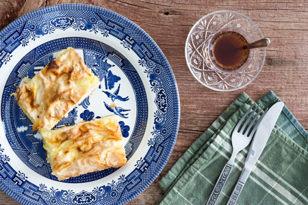 Slices of fresh homemade Turkish borek, a crisp light flaky phyllo or yufka pastry, served with a cup of traditional Turkish tea on a wooden picnic table, view from aboveの写真素材