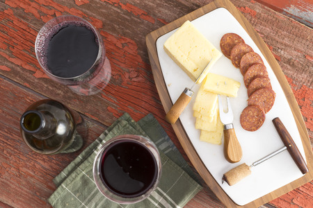 Bottle of red wine with two full glasses served with sliced harvati cheese and spicy sausage as a tasty appetizer to dinner on a rustic wooden table, overhead viewの写真素材