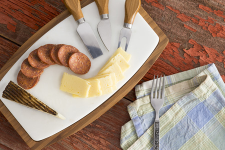 Overhead view of a cheeseboard with sliced Manchego cheese, a sheeps milk cheese from Spain, with spicy cured sausage served with a set of cheese cutters for a delicious appetizer before a mealの写真素材