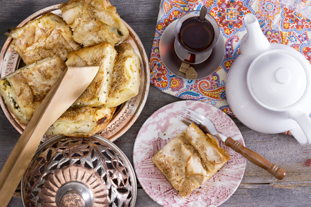View from above of a serving of delicious picnic eats with slices of borek on an authentic domed plate and Turkish tea on an old wooden picnic tableの写真素材