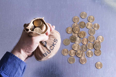 Man holding a money bag full to overflowing of Bucks with American dollar coins lying strewn on the...