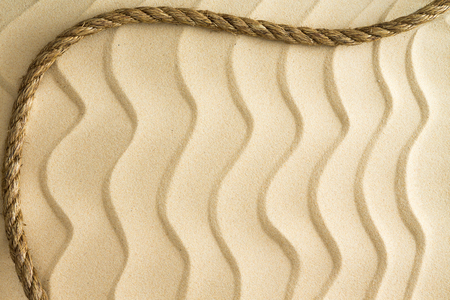 Nautical background of wavy golden beach sand with a ripple effect with a decorative curving rope border and copyspaceの写真素材