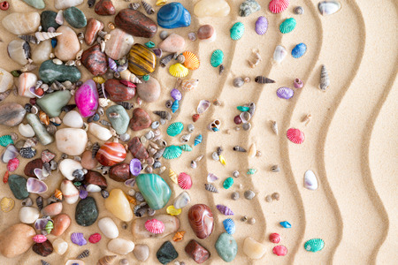 Pebbles, gemstones and shells scattered in a decorative arrangement on tropical golden beach sand with a ridged undulating wavy pattern in an ornamental nautical backgroundの写真素材