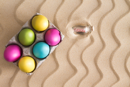 Traditional Easter Egg hunt on a tropical beach with colorful painted eggs hidden on the golden sand with a decorative squiggly wavy pattern of ridged lines with copyspaceの写真素材