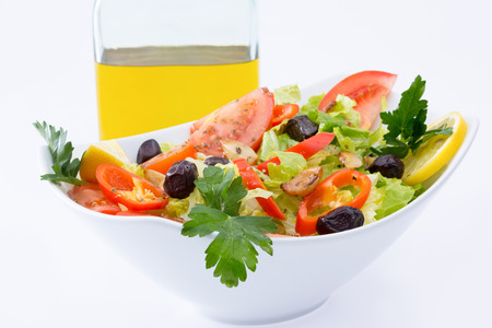 Fresh Mediterranean salad with olives, tomatoes, parsley, lemon, peppers, lettuce with extra virgin olive oil in the backgroundの写真素材