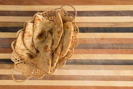 Delicious crusty whole grain naan flatbread slices, a leavened bread cooked in a tandoor clay oven, served in a decorative wicker basket on striped cutting boardの写真素材