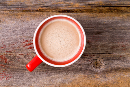 Orange ceramic mug full of fresh hot latte morning coffee topped with a milky froth の写真素材