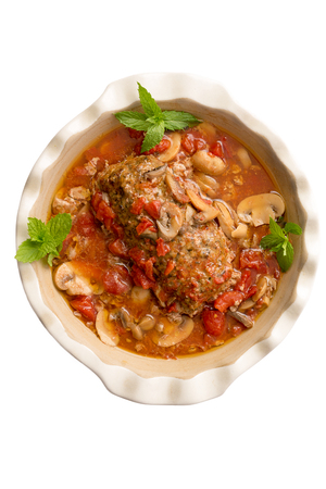 Gourmet meatloaf in a savory sauce with mushrooms and vegetables served in a white casserole , overhead view isolated on whiteの写真素材