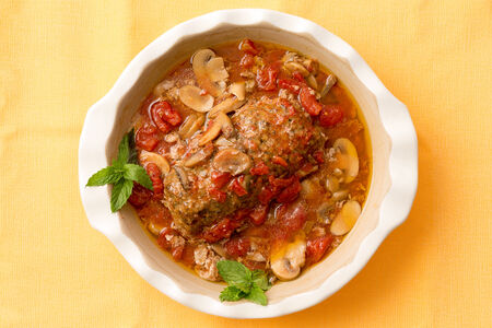 Delicious savory meatloaf in a casserole with mushrooms and vegetables garnished with mint on a yellow table cloth in a restaurant, overhead view with the dish centeredの写真素材