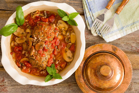 Sliced savory meatloaf with mushrooms and vegetables served in a casserole on a rustic wooden table with grungy peeling red paint, overhead view, copy space on the leftの写真素材