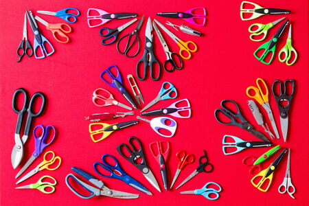 Display of multiple different pairs of domestic scissors on red conceptual of scissors for everyone and for every different task, overhead viewの写真素材