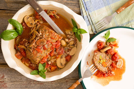 Sliced savory meatloaf with mushrooms and vegetables served in a casserole on a rustic wooden table with grungy peeling red paint, overhead view, copy space on the leftの写真素材