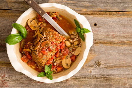 Sliced savory meatloaf with mushrooms and vegetables served in a casserole on a rustic wooden table with grungy peeling red paint, overhead view, copy space on the leftの写真素材