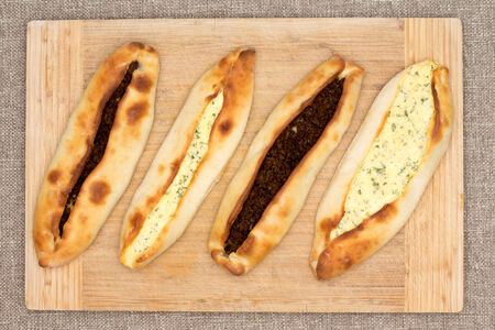Four traditional baked Turkish pide, an unleavened flatbread topped with savory ground beef meat and cheese and served on a wooden cutting board, overhead viewの写真素材