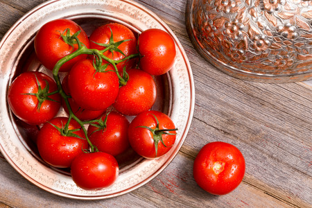 Farm fresh ripe red juicy tomatoes in a copper dish on a wooden table with the ornate lid alongside for healthy cooking and salad ingredients, view from aboveの写真素材