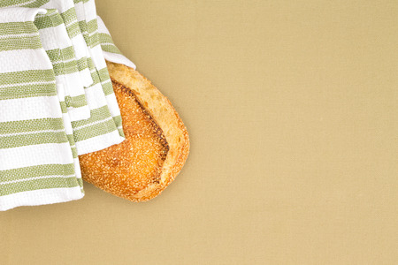 Crusty golden sesame seed bread loaf wrapped in a striped country cloth on a beige table cloth,...