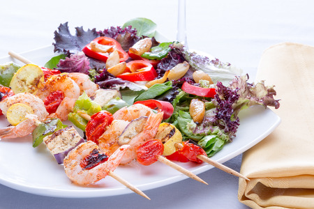 Shrimp skewers with bell pepper and tomato served with a fresh mixed salad for a delicious seafood dinnerの写真素材