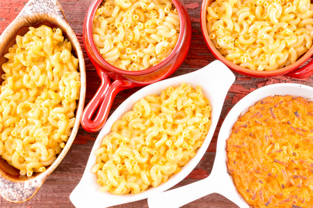 Conceptual above close view of cheese macaroni served in five diffrent cups on brown table clothの写真素材