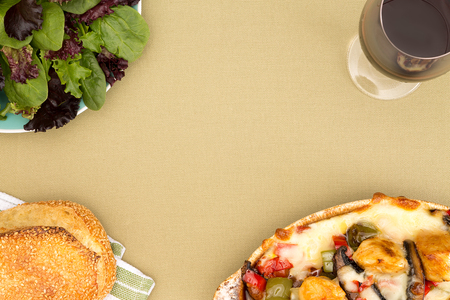 Chicken casserole, fresh salad, sesame bread and wine arranged in the corners of the frame to form a border with central copyspace on a beige table cloth viewed from aboveの写真素材