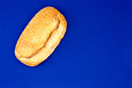 Freshly baked golden sesame seed bread with a crispy crust displayed diagonally across one corner on a bright blue backgroundの写真素材