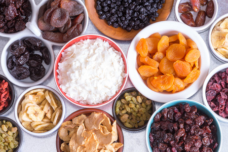 View from above of an assortment of dried fruit in individual dishes with apple, coconut, banana, apricots, raisins,cranberries, goji berries and prunesの写真素材