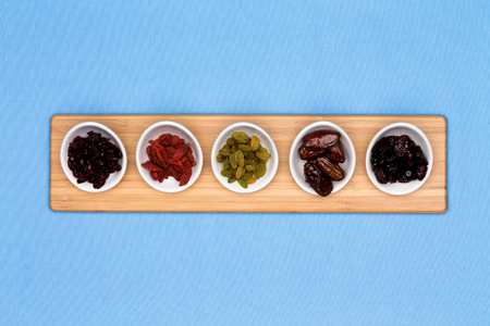 Dried fruits in individual containers on wooden tray on light blue backgroundの写真素材