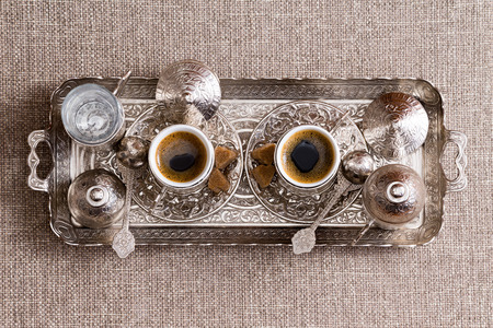 Traditional ornate metal tray with two matching cups of freshly brewed Turkish coffee with sugar, lids and a pot or cezve viewed from aboveの写真素材