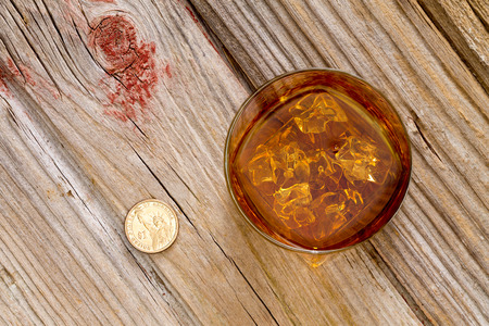 Glass of whiskey and a coin for a gratuity or tip standing on an old textured wooden bar counter, view from above with copyspaceの写真素材