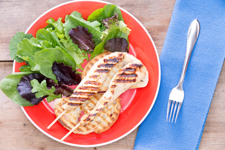 Grilled meat served with leaf vegetables served on a red plateの写真素材