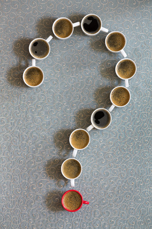 White coffee mugs filled with milky freshly brewed coffee arranged as a question mark with a single red cup as the point on a grey background in a conceptual image, viewed from aboveの写真素材