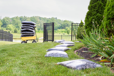 Mulching the garden takes time and effort with bags of mulch laid out on the lawn alongside the flowerbed in a long row waiting to be spread with a cart stacked full of bags in the backgroundの写真素材