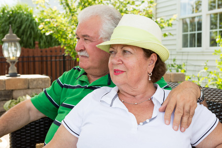 Elderly couple sitting on a wicker settee on an outdoor patio gazing into the distance watching something with serious expressionsの写真素材