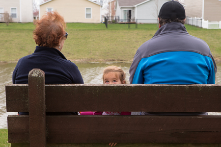 Small Family Sitting on a Wooden Bench at the Park Looking Different Directions.の写真素材