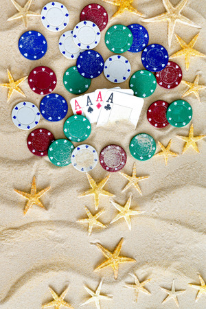 Gambling on Vacation Concept - White Sand with Yellow Stars, Colored Poker Chips and Four Ace Cards.の写真素材