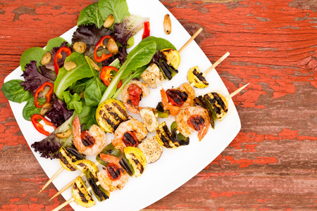 Appetizing Gourmet Shrimp Skewers Served on White Plate with Veggies and Spices on Top of a Rustic Wooden Tableの写真素材