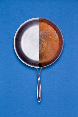 New coated non-stick and old rusted frying pan combined into one halved unit for comparison of age and condition in a conceptual overhead view on a blue backgroundの写真素材