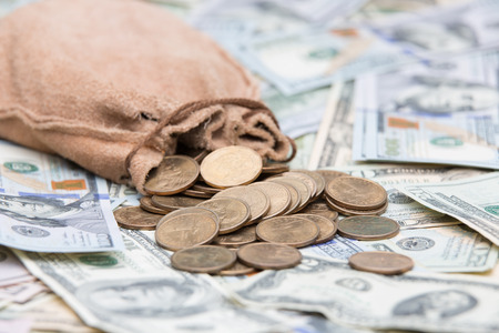 Golden dollar coins spilling from a hessian bag onto a background of US dollar bills with focus to the coins conceptual of wealth, winnings, growth returns, success, graft or money laundering conceptの写真素材