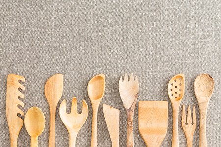 Border of wooden kitchen necessities with the heads of assorted utensils in a row along the bottom of the frame on a beige textile background with copyspaceの写真素材