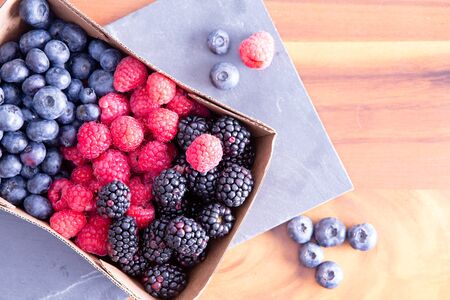 Box of fresh seasonal autumn berries with blueberries, blackberries, and raspberries displayed in a...