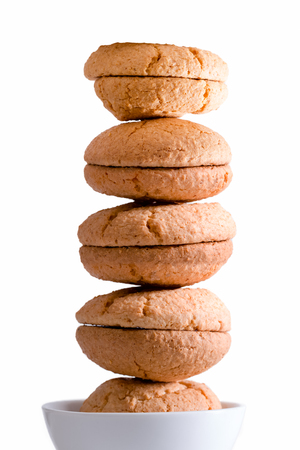 Neatly stacked tower of freshly baked macaroons balancing in a bowl centered over a white background, side litの写真素材